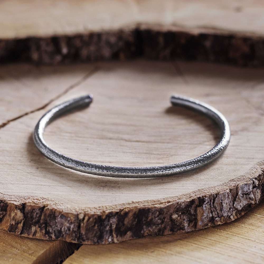 Thin Cuff Bracelet with a Frosted Finish in Dark Silver on a wooden background
