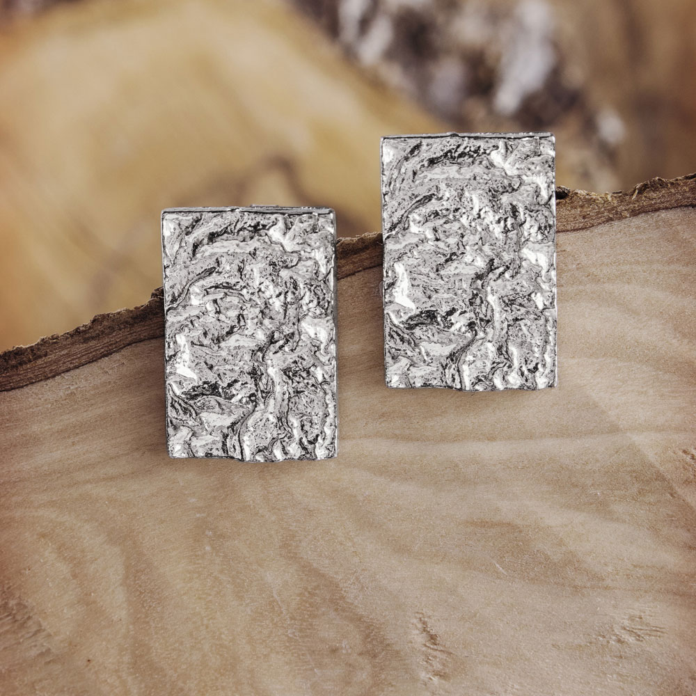 A Pair of Square Stud Earrings with a Textured Surface on a Wooden Background