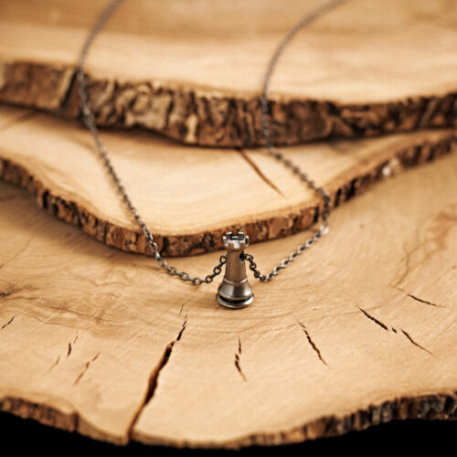 Rook Chess Piece Pendant Necklace in Oxidized Solid Silver laid down on a log