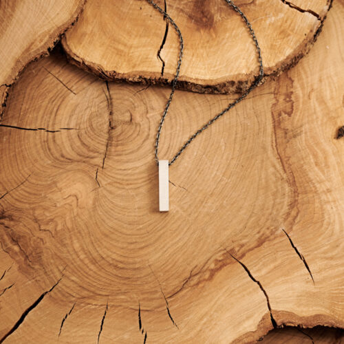Engravable Bar Pendant Necklace in Sterling Silver laid down on a log