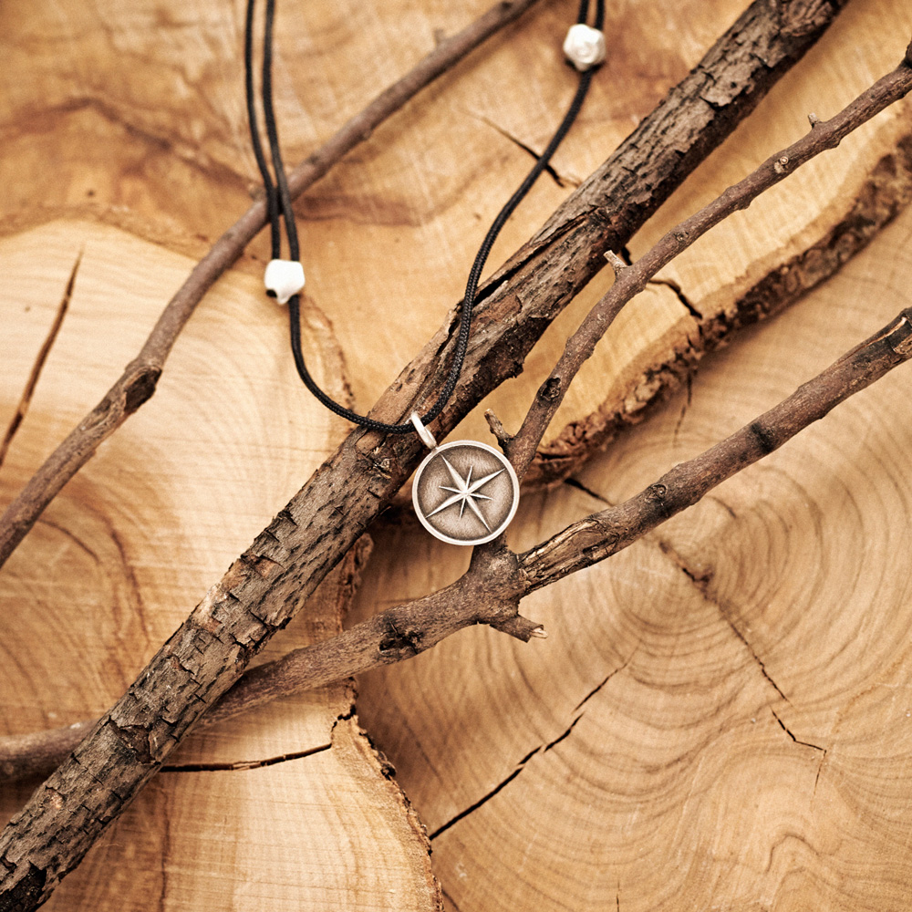 Silver Compass Pendant Necklace with an Oxidized Finish with a black cord laid down on a log