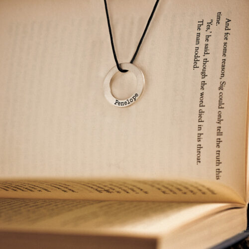 Sterling Silver Personalized Necklace with a Circle Pendant and a black cord beautilfully displayed hanging from a book