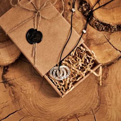 A Three Ring necklace with a black cord displayed inside the box that it comes with displayed on a log