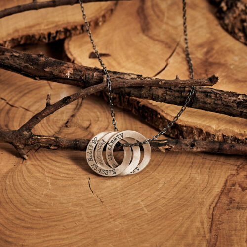 A strerling silver Three Ring necklace laid down on a log