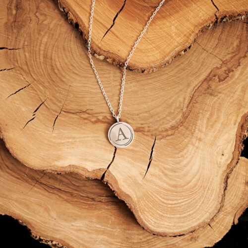 Initial Round Pendant Necklace in Sterling Silver with a chain laid down on a log
