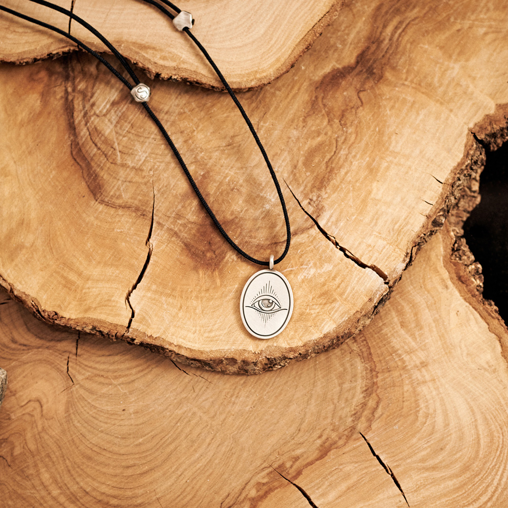 Oval Shaped All-Seeing Eye Necklace with a long black cord laid down on a log