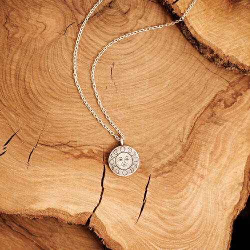 Sun Face Pendant Necklace in Oxidized Silver and a long chain laid down on a log