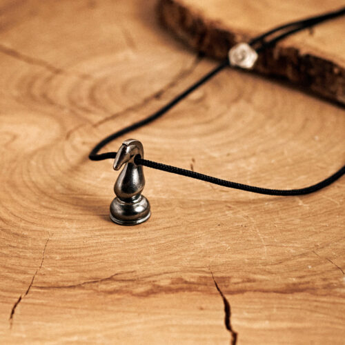 Knight Chess Piece Pendant Necklace in Dark Silver with a black cord laid down on a log