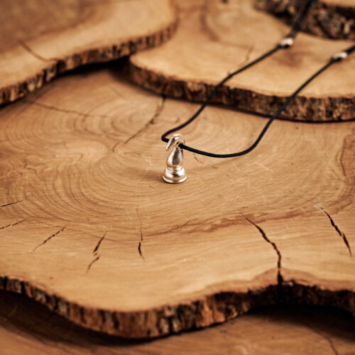 Knight Chess Piece Necklace in Sterling Silver with a black cord laid down on a log