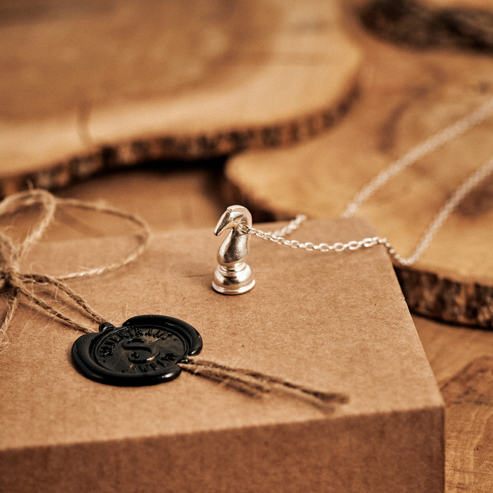 Knight Chess Piece Necklace in Sterling Silver with a chain laid down on a log