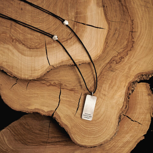 A personalized tag pendant with a black cord necklace in sterling silver beautifully displayed on top of a log