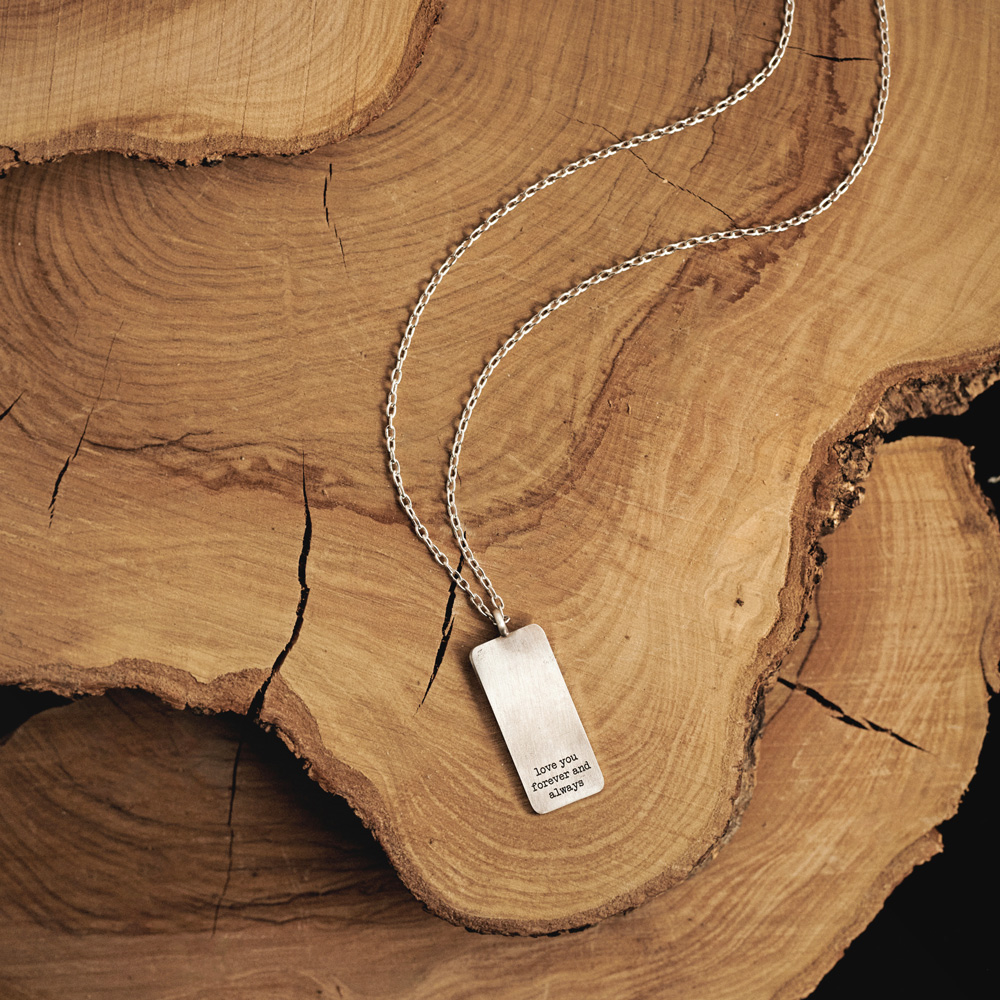 A personalized tag pendant necklace wth a chain in sterling silver beautifully displayed on top of a log