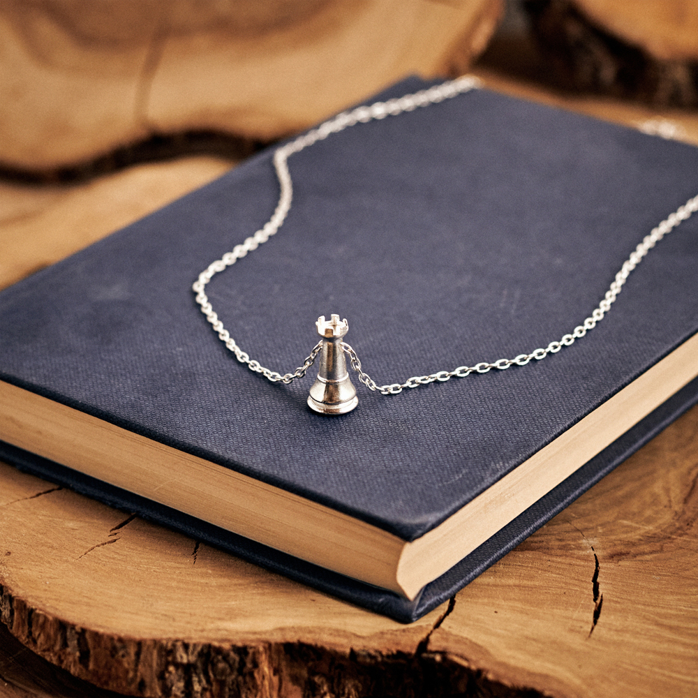 White Rook Chess Piece Necklace in Solid Sterling Silver with a chain displayed on top of a book.