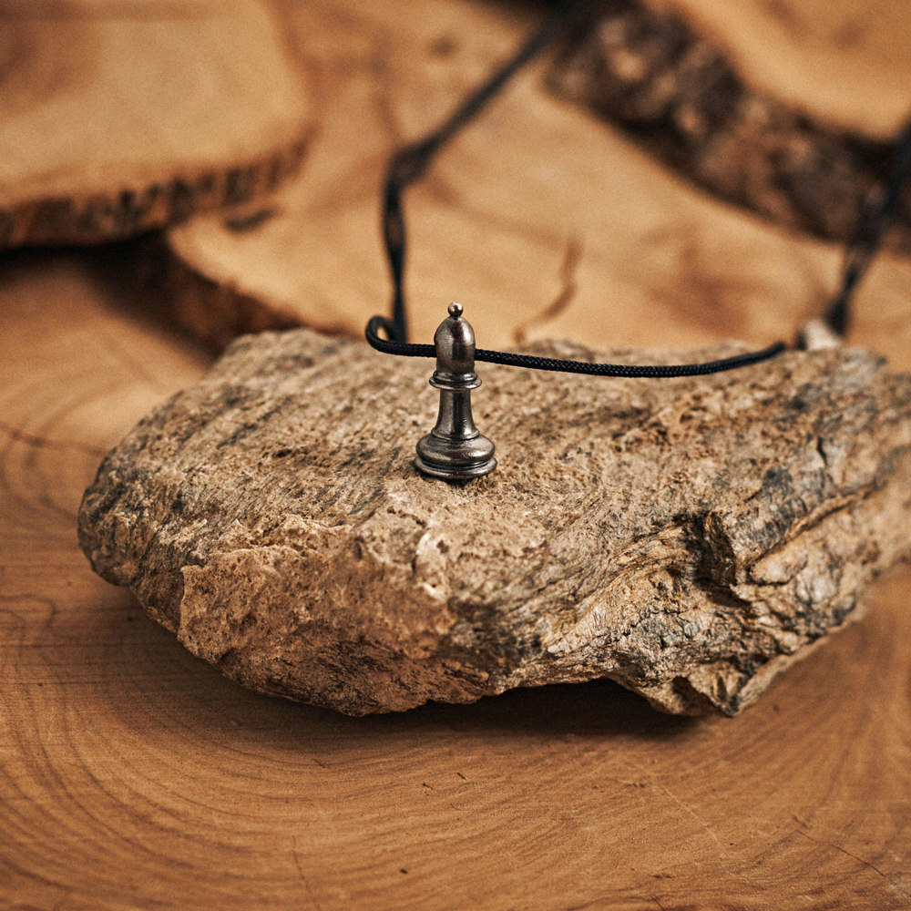 Black Bishop Chess Piece Necklace Sterling Silver with a black cord displayed on top of a rock.
