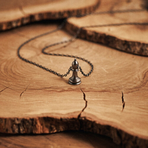 Black Bishop Chess Piece Necklace Sterling Silver displayed on top of a log.
