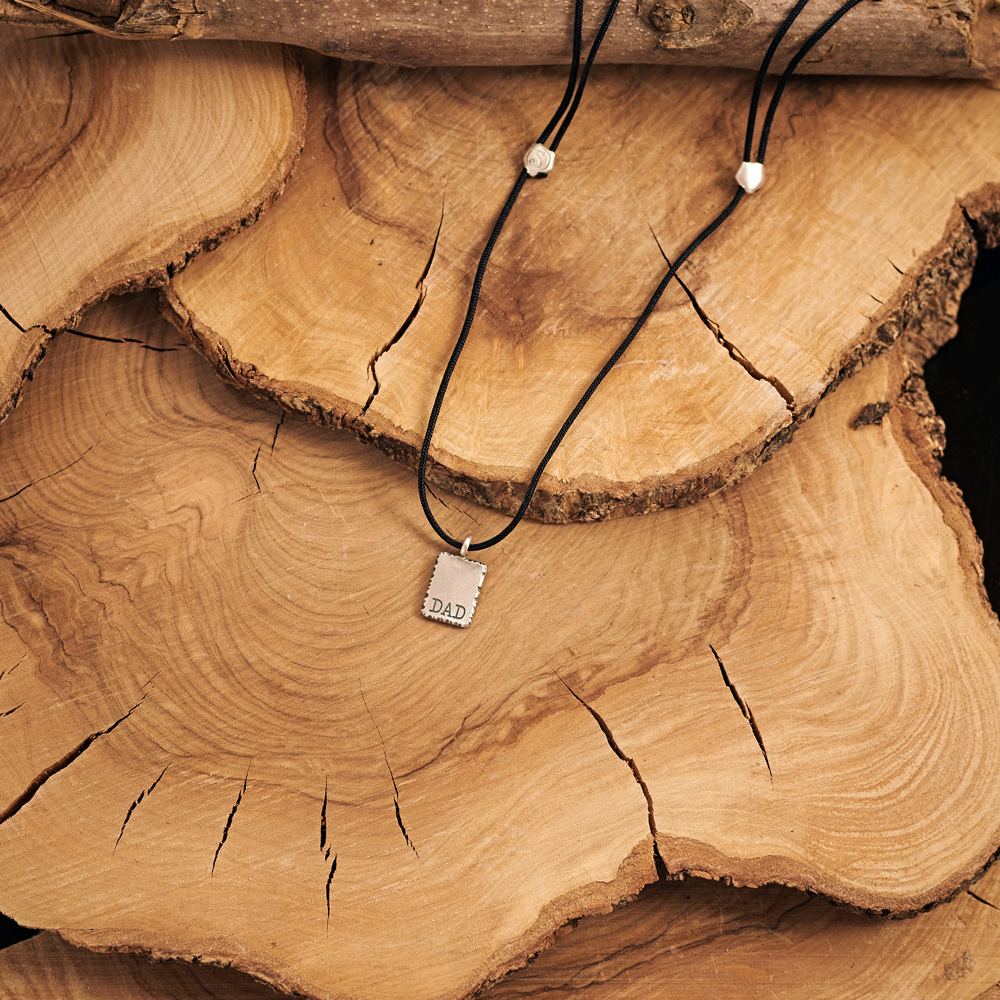 our sterling silver personalized dad pendant with a black cord displayed on a log.