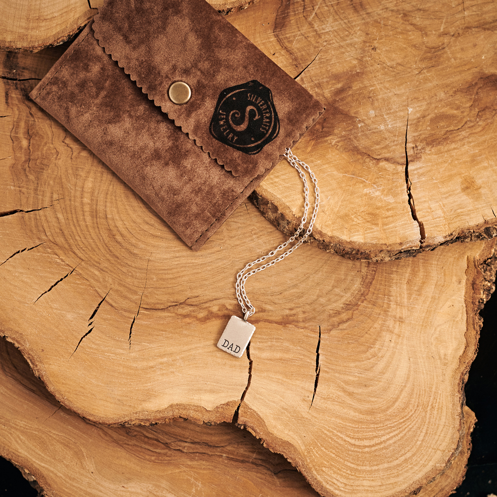 our sterling silver personalized dad pendant with a chain displayed on a log.