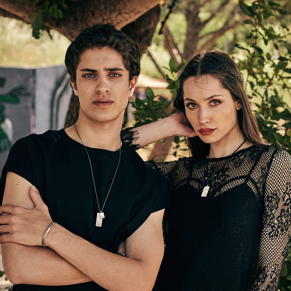 Both female and male models are posing wearing the two versions of the Personalised Double Small and Large Silver Pendant. A chain made of sterling silver or a black cord.